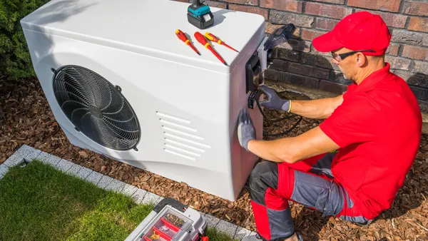 A man in a red uniform repairing a heat pump.