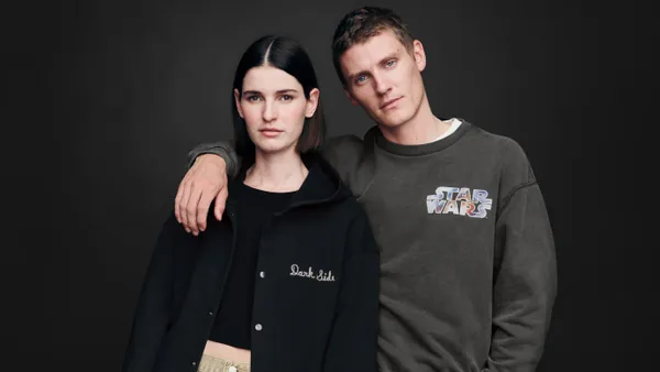 Two people stand against a dark background. One wears a brown T-shirt that reads "Star Wars" and the other wears a black hoodie that says "Dark Side"