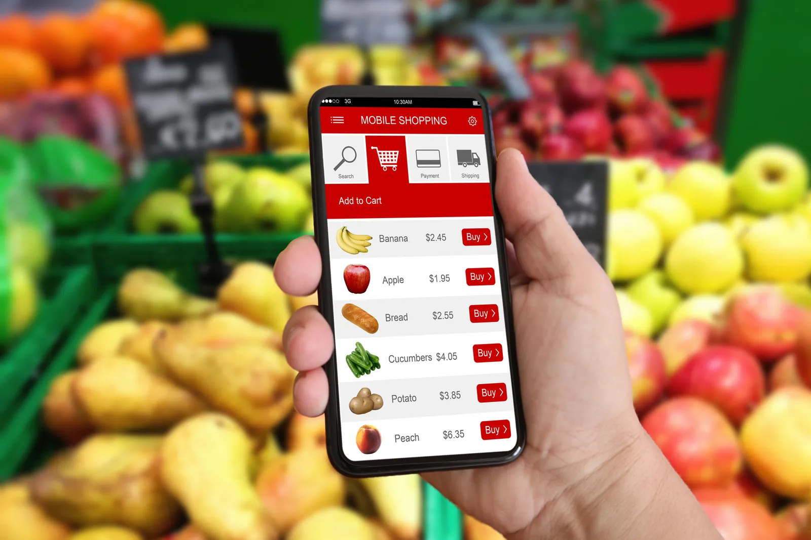 In front of a fruit display, a hand holds a phone with a grocery app open.