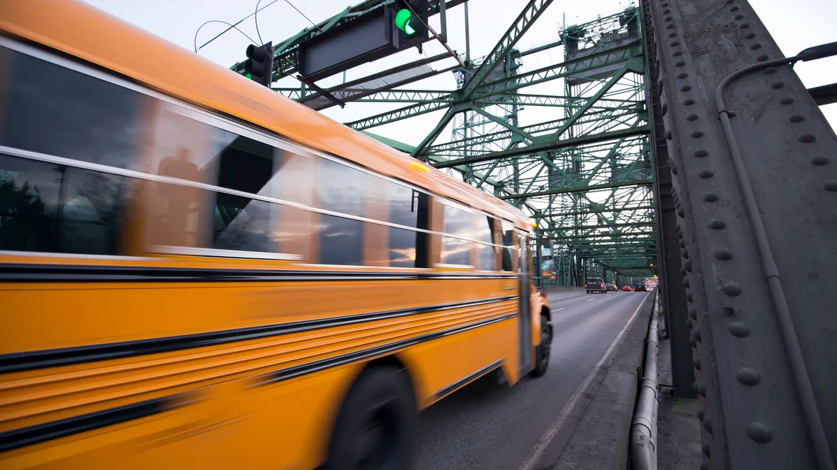 A school bus drives along a metal bridge under a green traffic light.