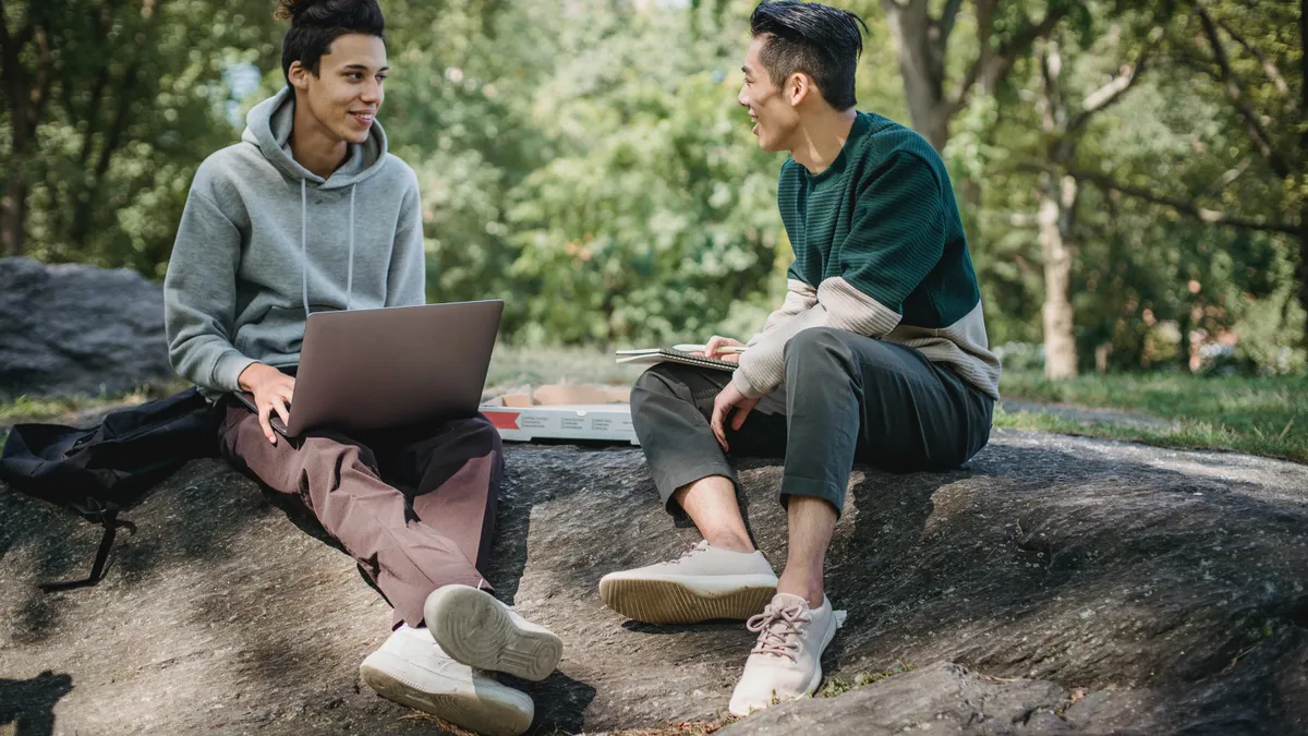 Two employees (one Asian, one Latinx) work together outside