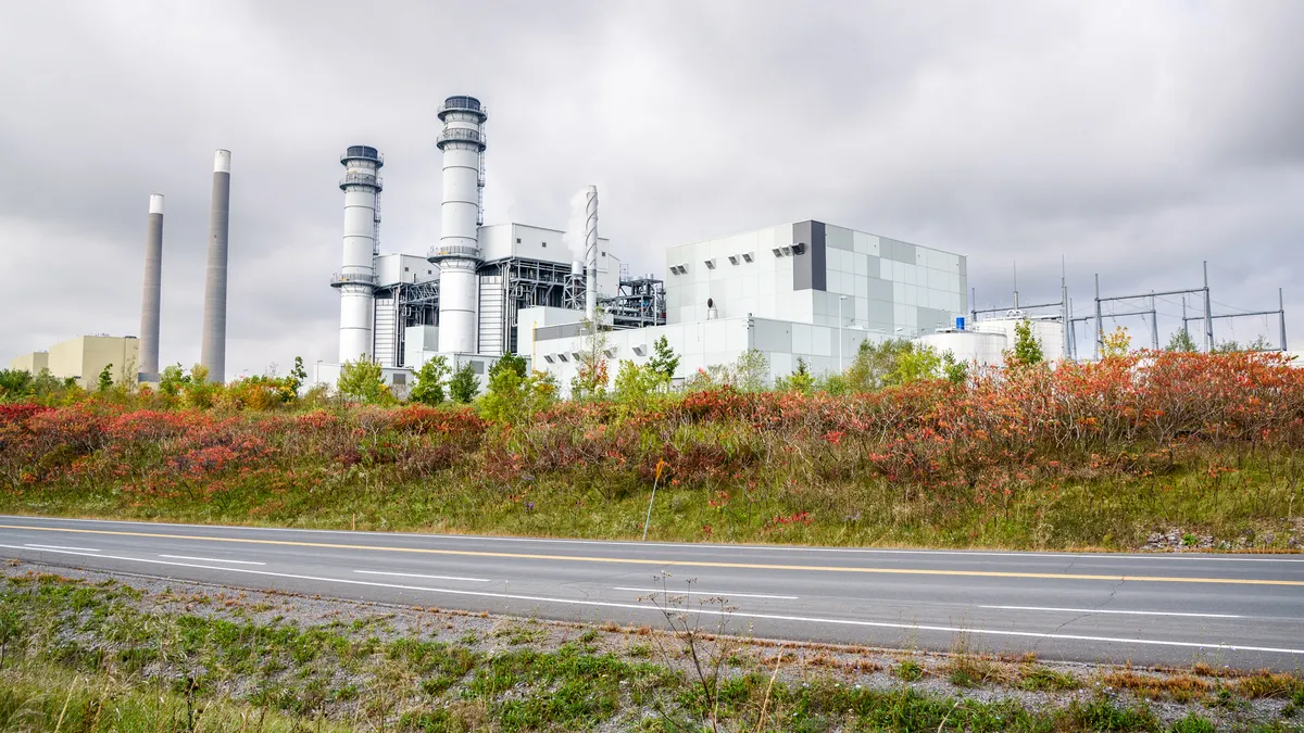 A gas-fired power plant with smokestacks overlooks a road.