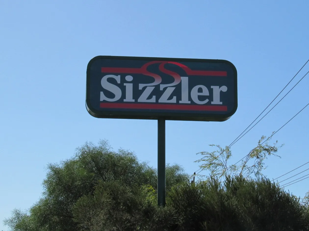 A green sign with white logo that says &quot;Sizzler&#x27; there are red lines above the words.