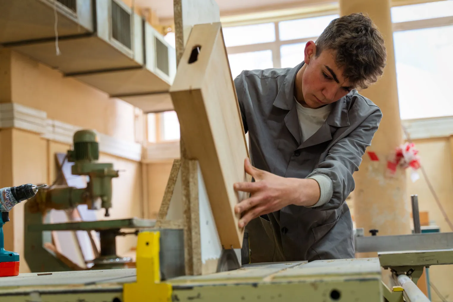 A high school-aged student performs carpentry work in a wood shop.