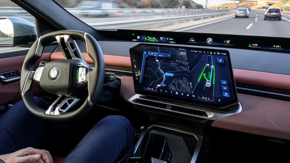 A human rides in the driver's seat of a new BMW iX3 50 xDrive, which is equipped with automated driving via the BMW Highway/Motorway-Assistant.