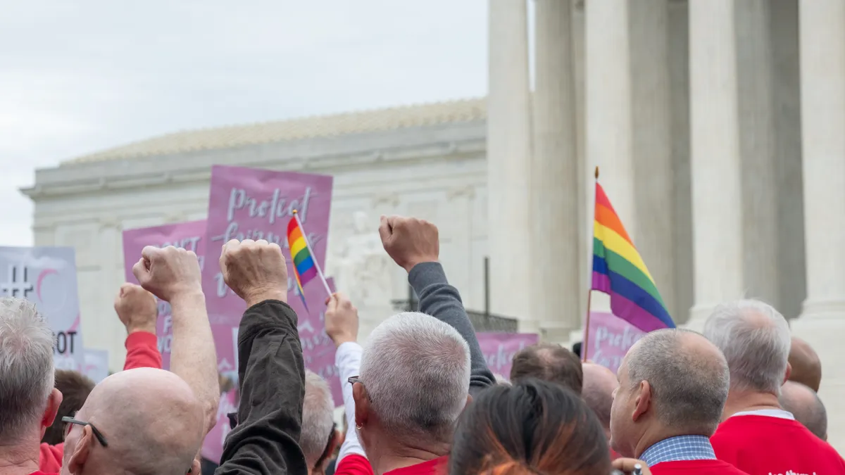 Individuals hold pride flags in front of the U.S. Supreme Court.