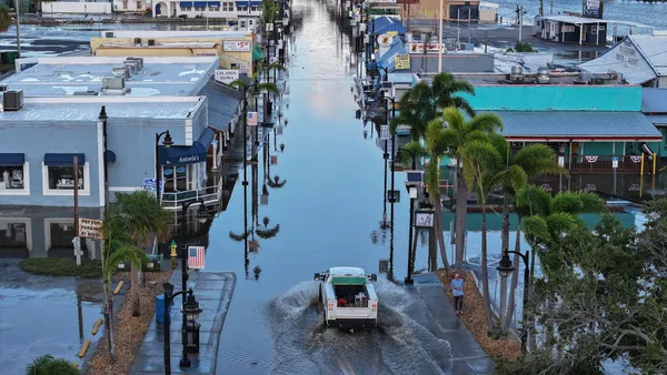 Aerial shot of flooded street lined by palm trees and houses. A truck drives down the flooded street.