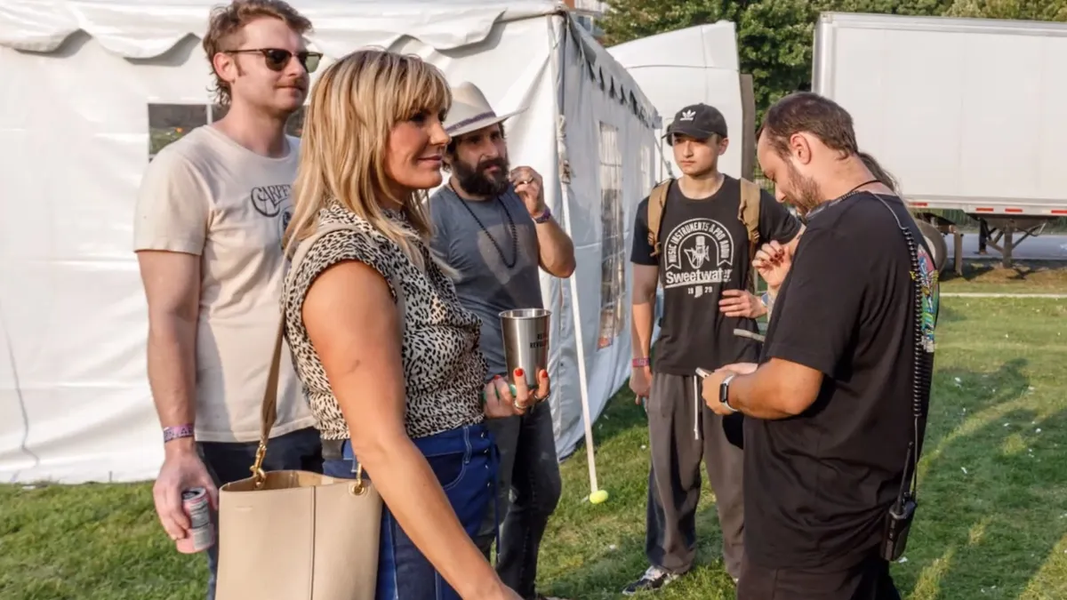 Grace Potter stands holding a metal cup with a crowd of people at a music event