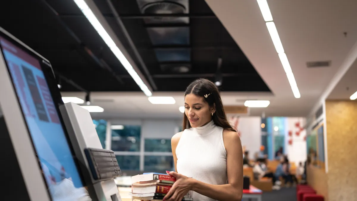 Young woman searching for a book in the library system at university