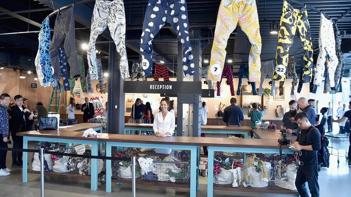 A G-Star Raw store is pictured, including a reception desk which showcases pairs of jeans above it. Customers walk around the desk.