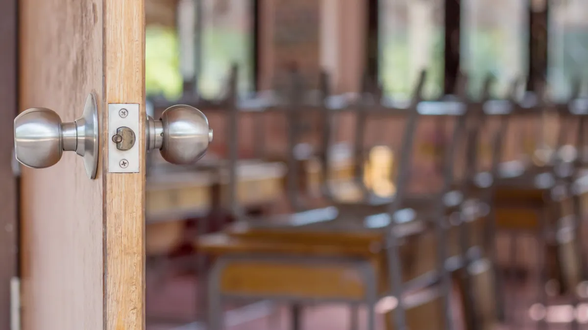 A door opens to an empty classroom with chairs flipped upside down on top of desks.