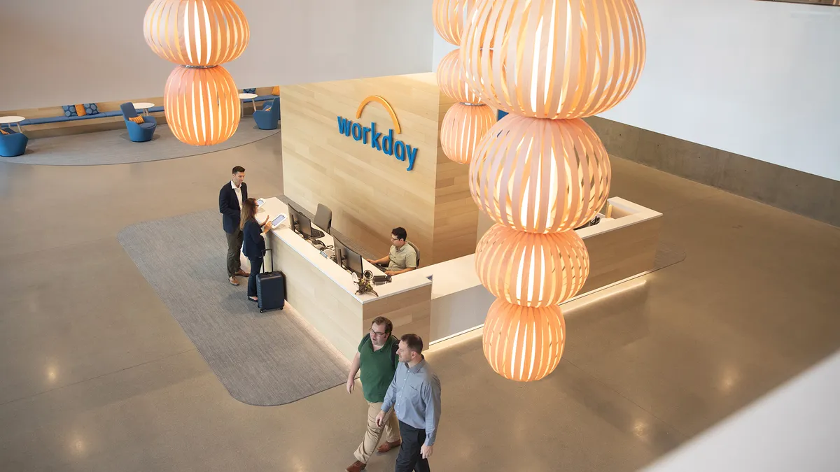 A lobby is pictured from above with a Workday sign displayed above a front desk area. Workers walk through the lobby and stand at the desk.