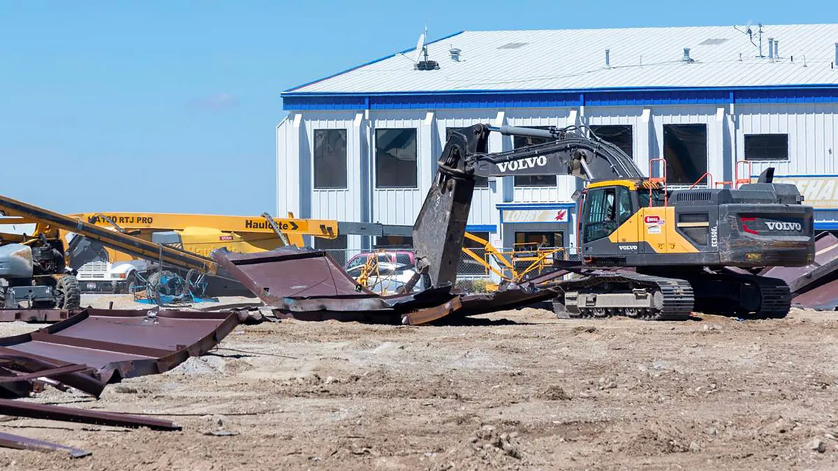 Construction machinery over a jobsite with broken and twisted debris.