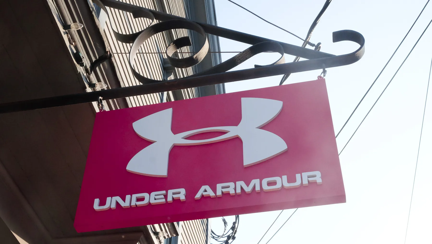 A red sign with a white logo and the words "under armour" in white capital letters hangs from an iron post.