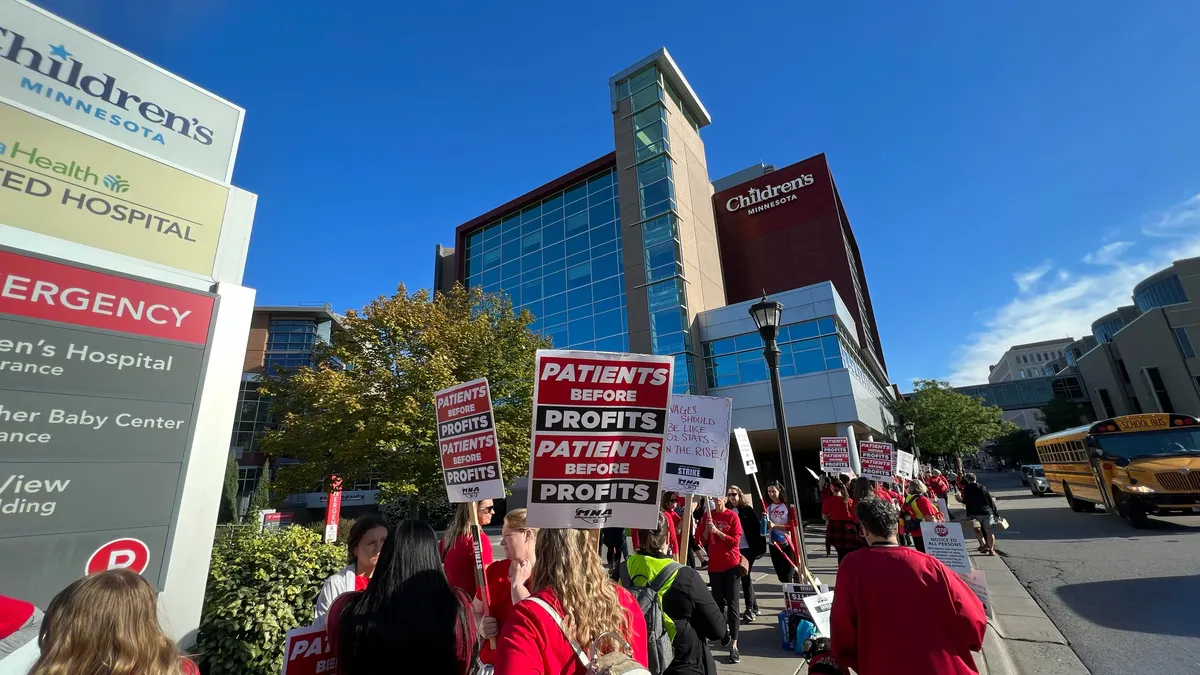 Nurses hold signs reading "patients before profits" while picketing outside a hospital.