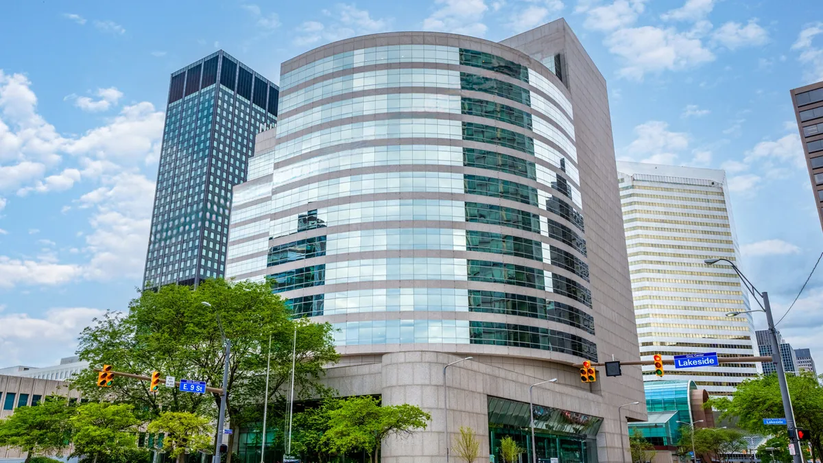 A shot from the ground on the street centers a circular building in the city. The building is modern, glassy and gray.