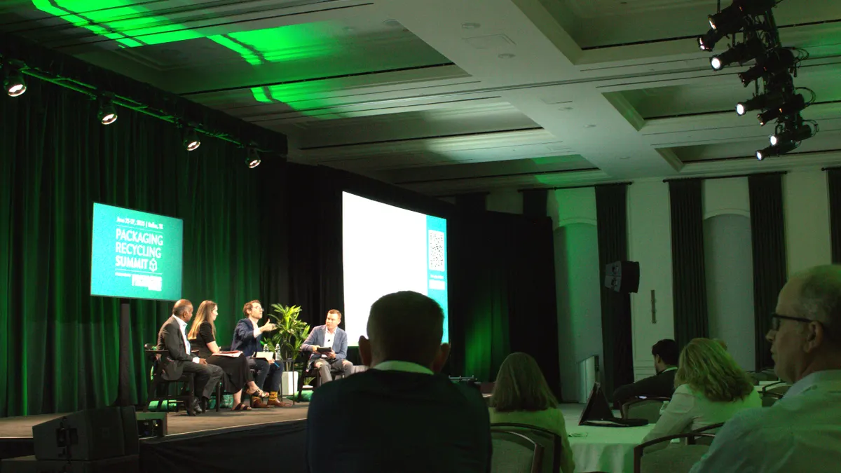 Audience members watch four speakers sitting on a stage in front of a green background that says Packaging Recycling Summit.