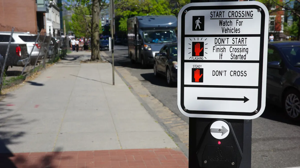 A sign at a crosswalk with a push button.