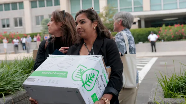 A person is carrying a box and looking ahead while walking away from a building.