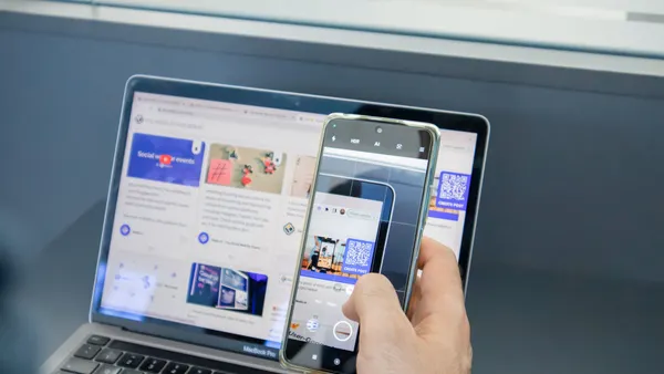 A person holding a cell phone in front of a laptop