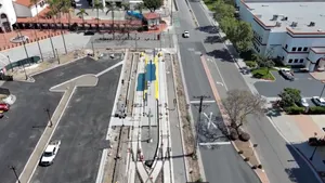 Overhead view of a street alongside two railroad tracks and a parking area with a red tile roofed train station.