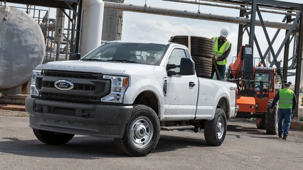 A person secures tires in the bed of a white 2021 F-250 Super duty pickup in an outdoor industrial setting.