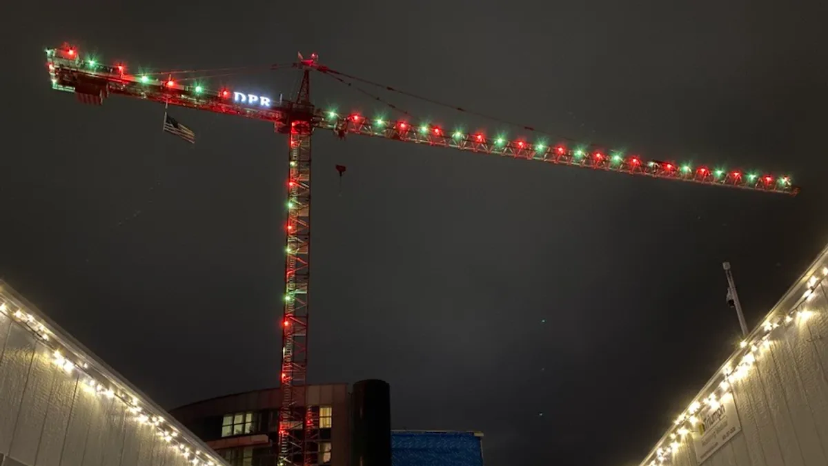 A shot from the ground of a lit-up crane, covered in holiday lights. It looms high in the night sky.