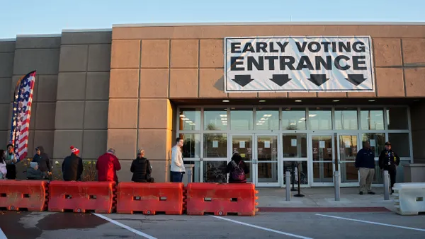 People standing in line in front of a building with a banner that reads Early Voting Entrance.