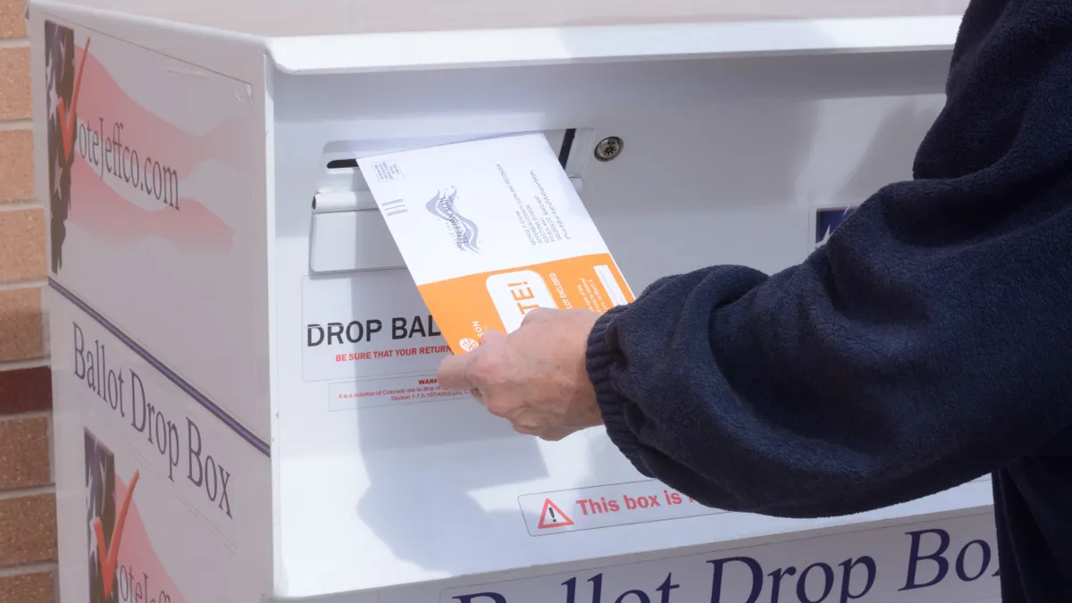 A person inserts an early election ballot envelope into a ballot drop box in Jefferson County, Colorado.