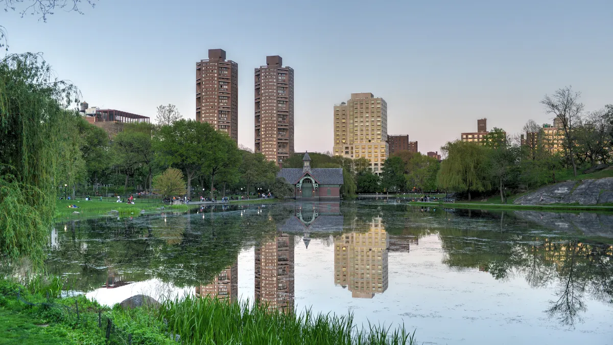 A water body surrounded by trees and green space with tall buildings in the background.