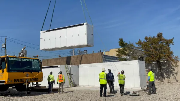 NineDot Energy workers watch as a crane lowers a battery unit.