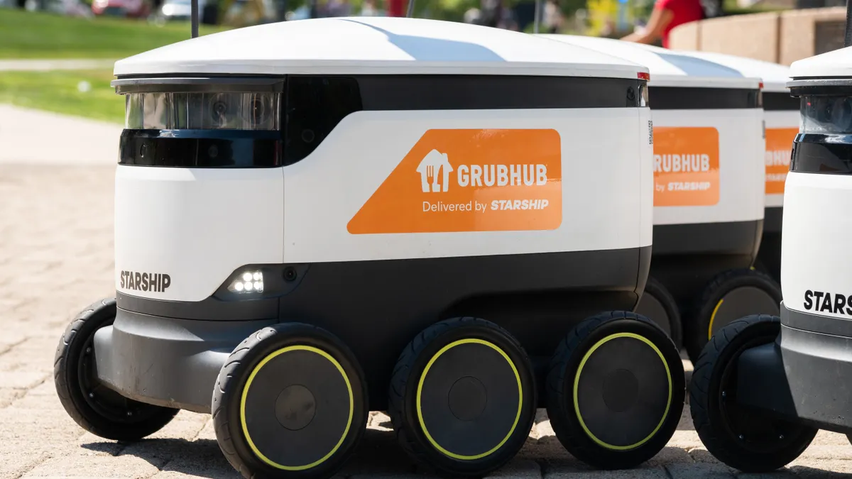 A picture of a white delivery robot with an orange Grubhub logo on the side