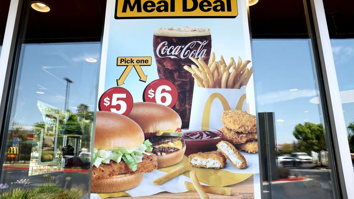 Am image of a sign on a window that says "Meal Deal" and shows a chicken sandwich and burger with nuggest, fries and a Coca-Cola.