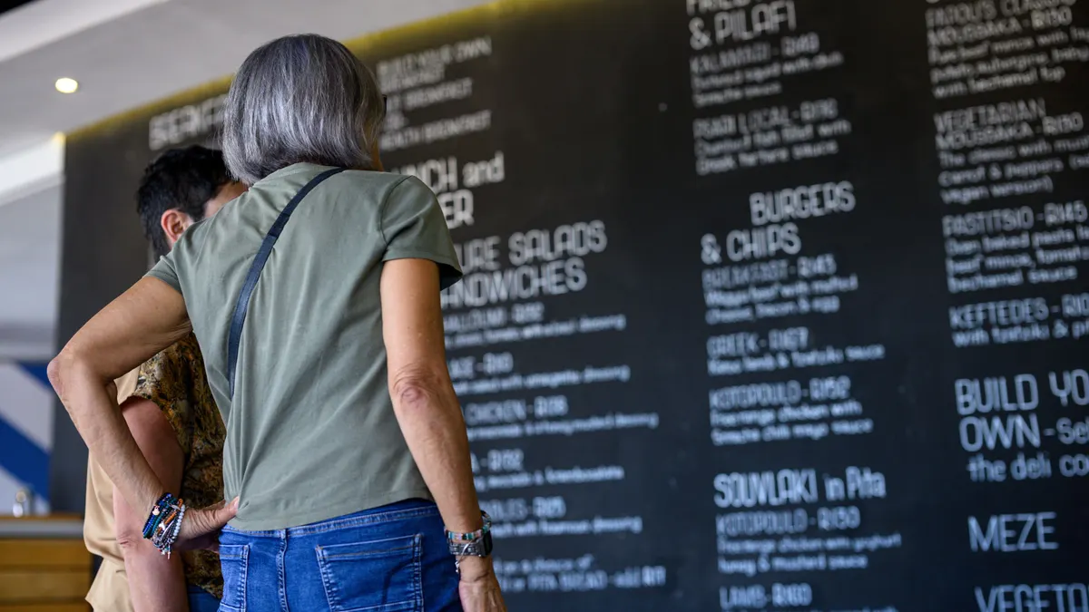 A photograph of two people in the foreground looking at a chalkboard menu that is blurred