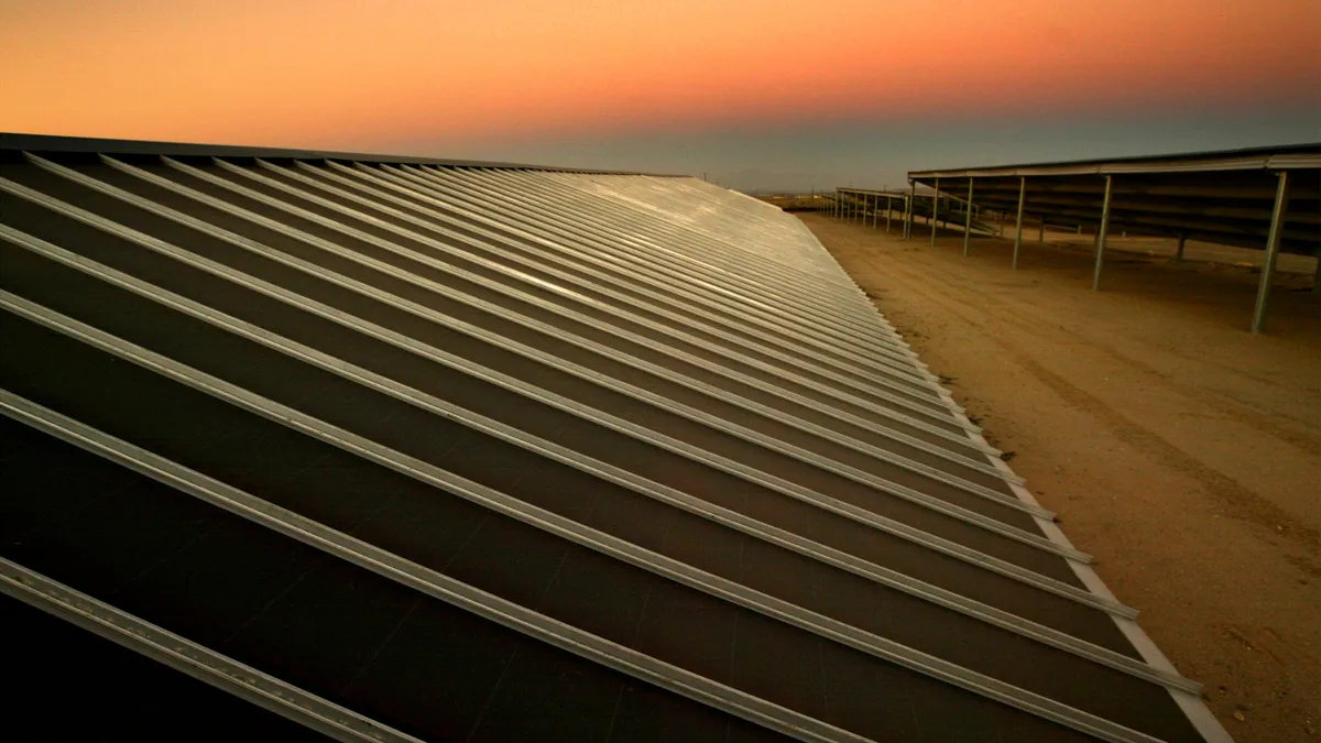 Solar panels sit on a beach at sunset.