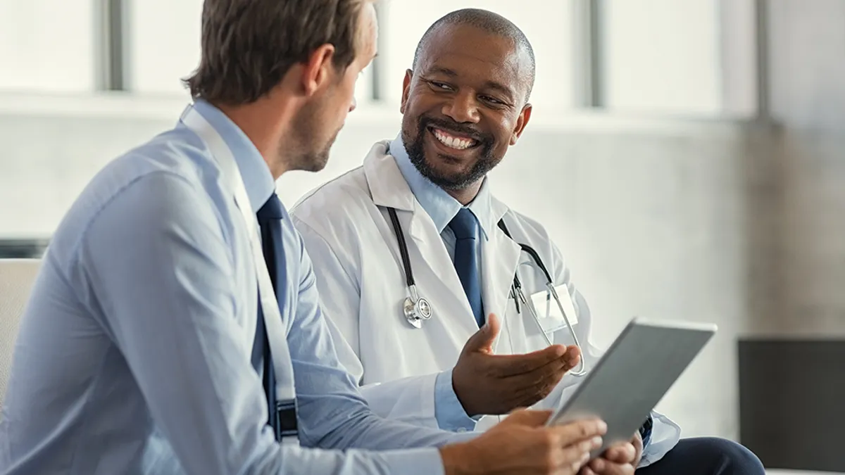 Two mature smiling doctors having discussion about patient diagnosis, holding digital tablet.