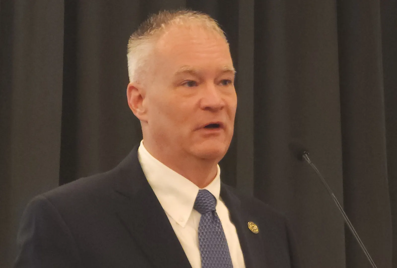 A man in a suit speaking into a microphone.