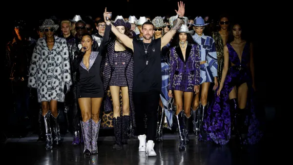 Philipp Plein raises his arms on the runway infront of a group of models wearing clothing from the Philipp Plein brand.