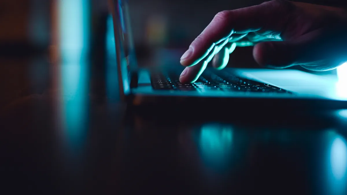 A hand typing on a laptop against a dark backdrop