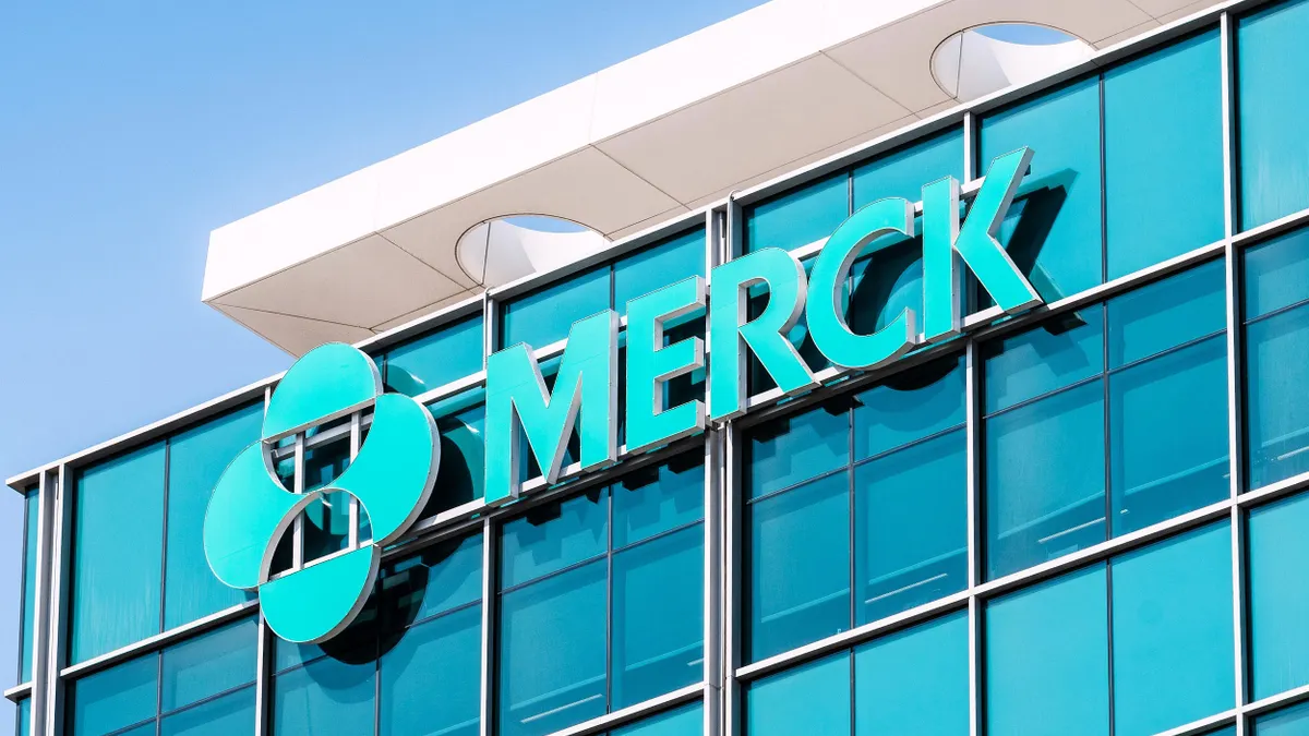 An all-green glass building facade with a logo that reads "MERCK" is displayed on the exterior of the research facility. 