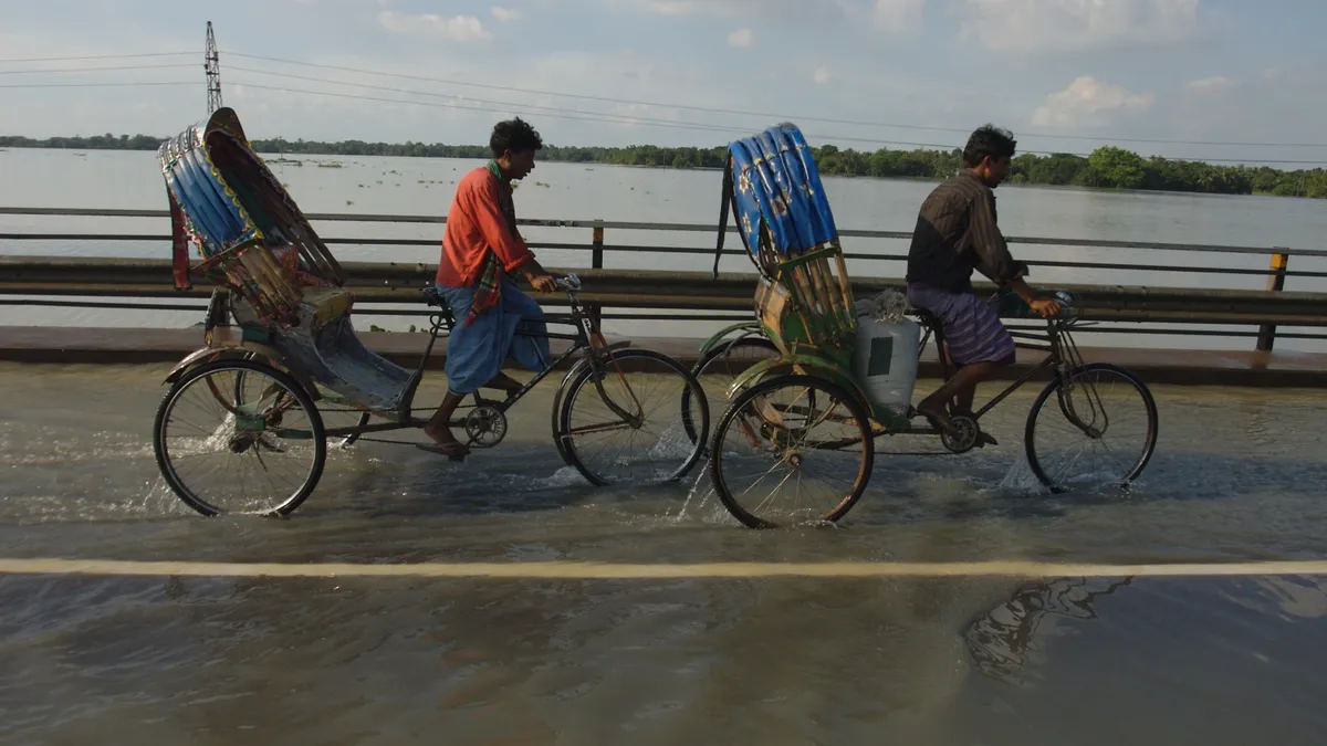 A group of Bangladesh residents ride bikes across a bridge which has flooding.