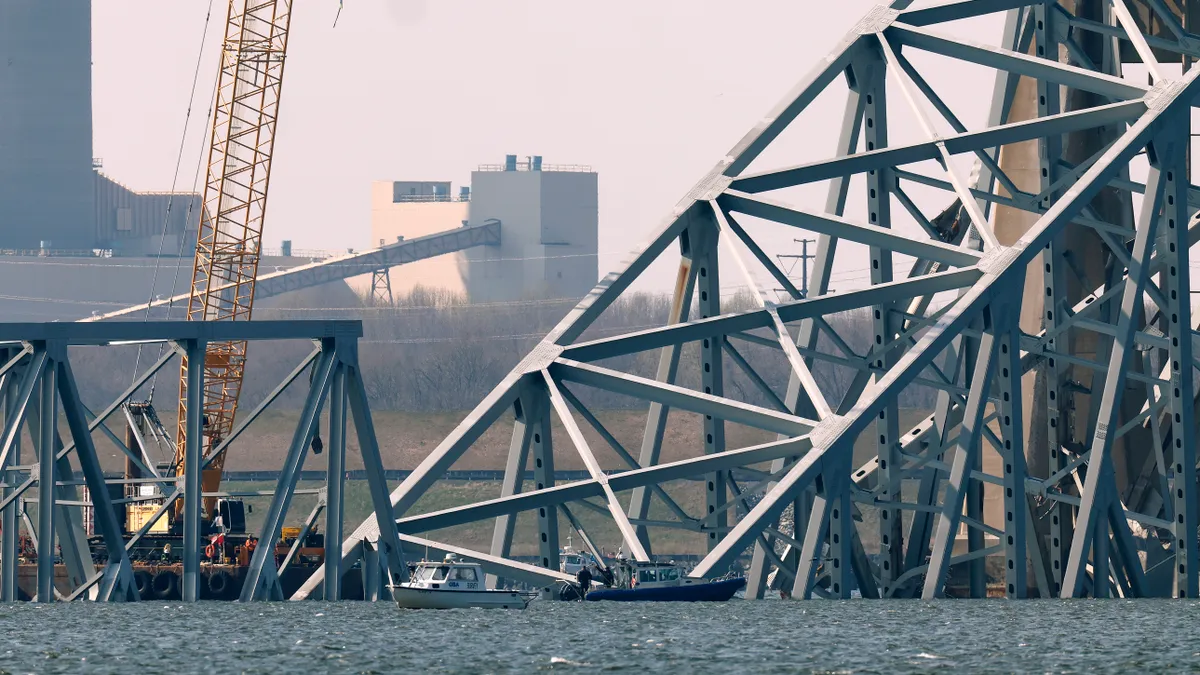 A yellow crane is dwarfed by massive broken steel debris from a bridge.