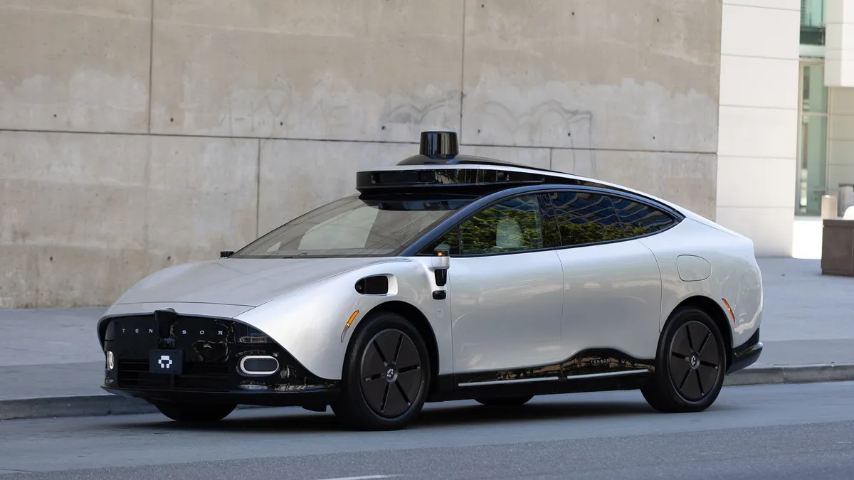 A silver Tensor RoboCar parked in front of a concrete wall.