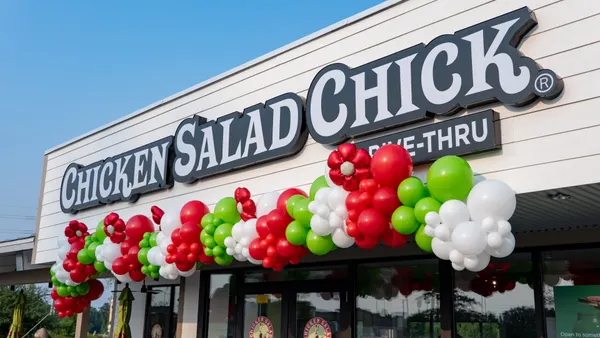 An photograph of a building sign that says Chicken Salad Chick drive-thru with red and green balloons underneath.