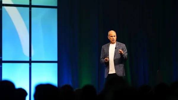 a man in a suite speaks on stage before a silhouetted crowd