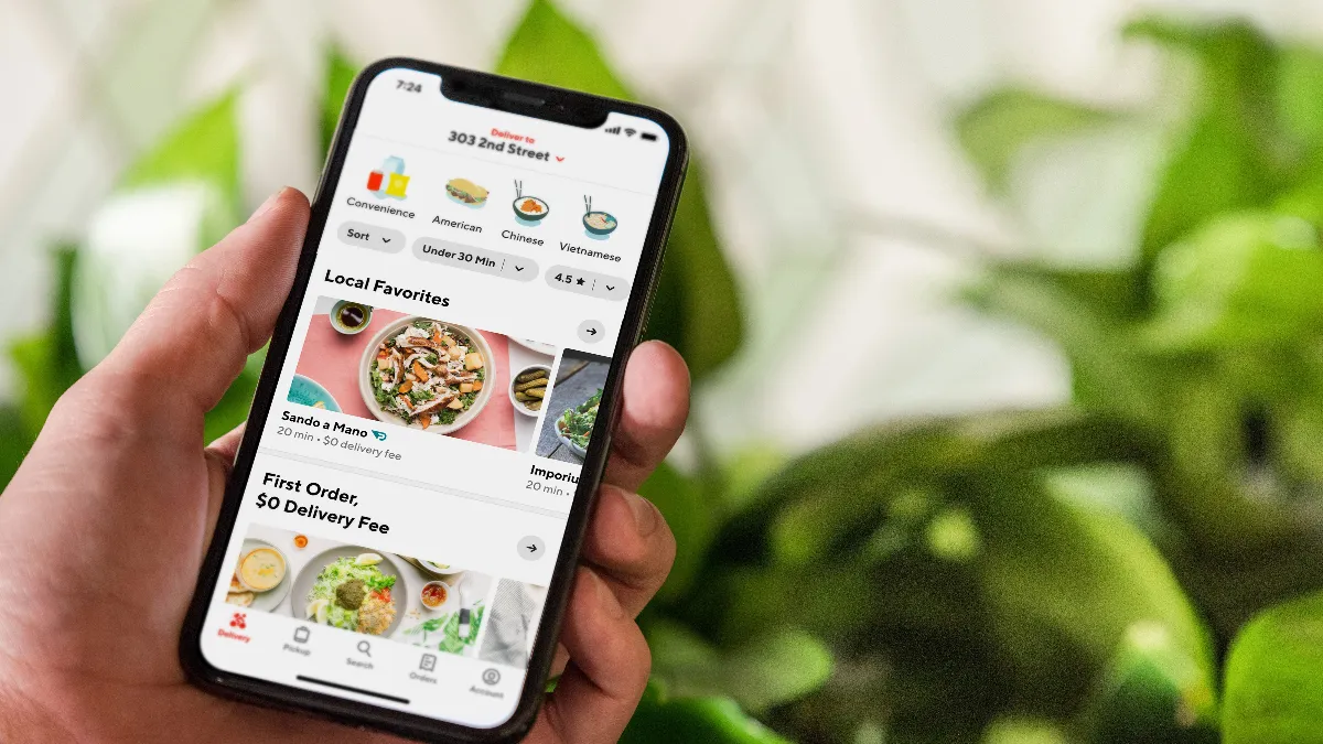 An image of a hand holding a smart phone with the DoorDash homepage.