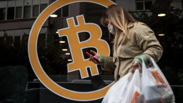 Person with shopping bag passes storefront window with Bitcoin sign