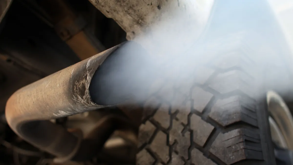 Close-up of a vehicle tailpipe spewing out gray emissions.