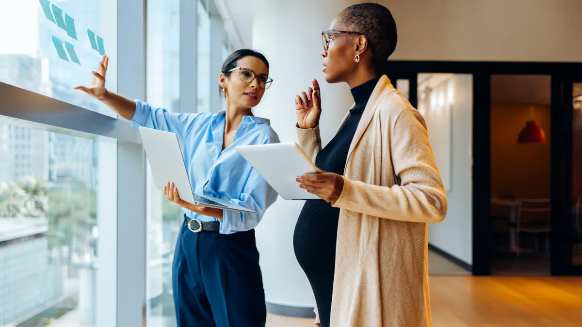Two professional women discussing ideas and using technology in an office setting
