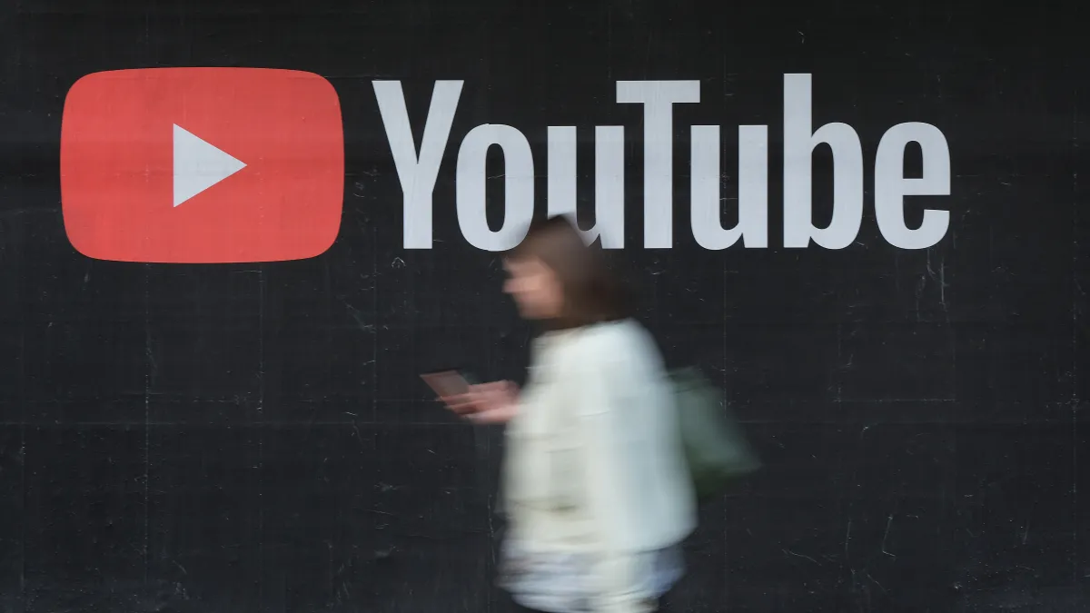 A young woman with a smartphone walks past a billboard advertisement for YouTube on Sept. 27, 2019, in Berlin, Germany.